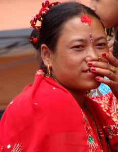 A married Nepali woman wearing red sari, vermillion hair stripe, and tika dot (red nails too.)